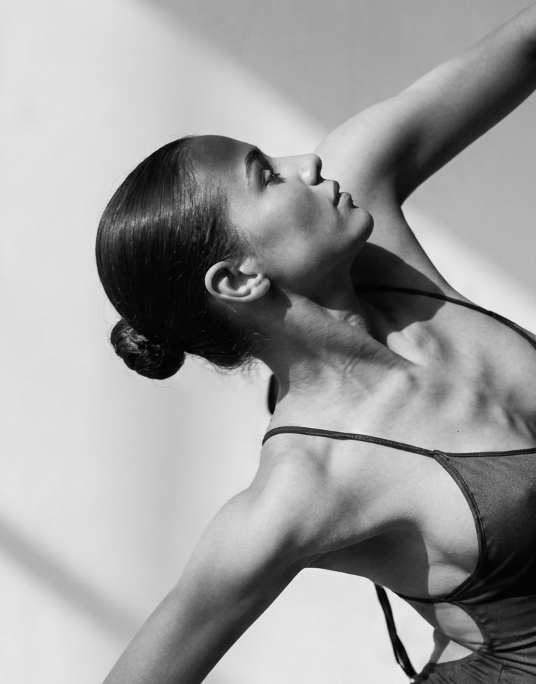 Black and white editorial photograph of a dancer in a vinyasa pose, bright minimalist studio