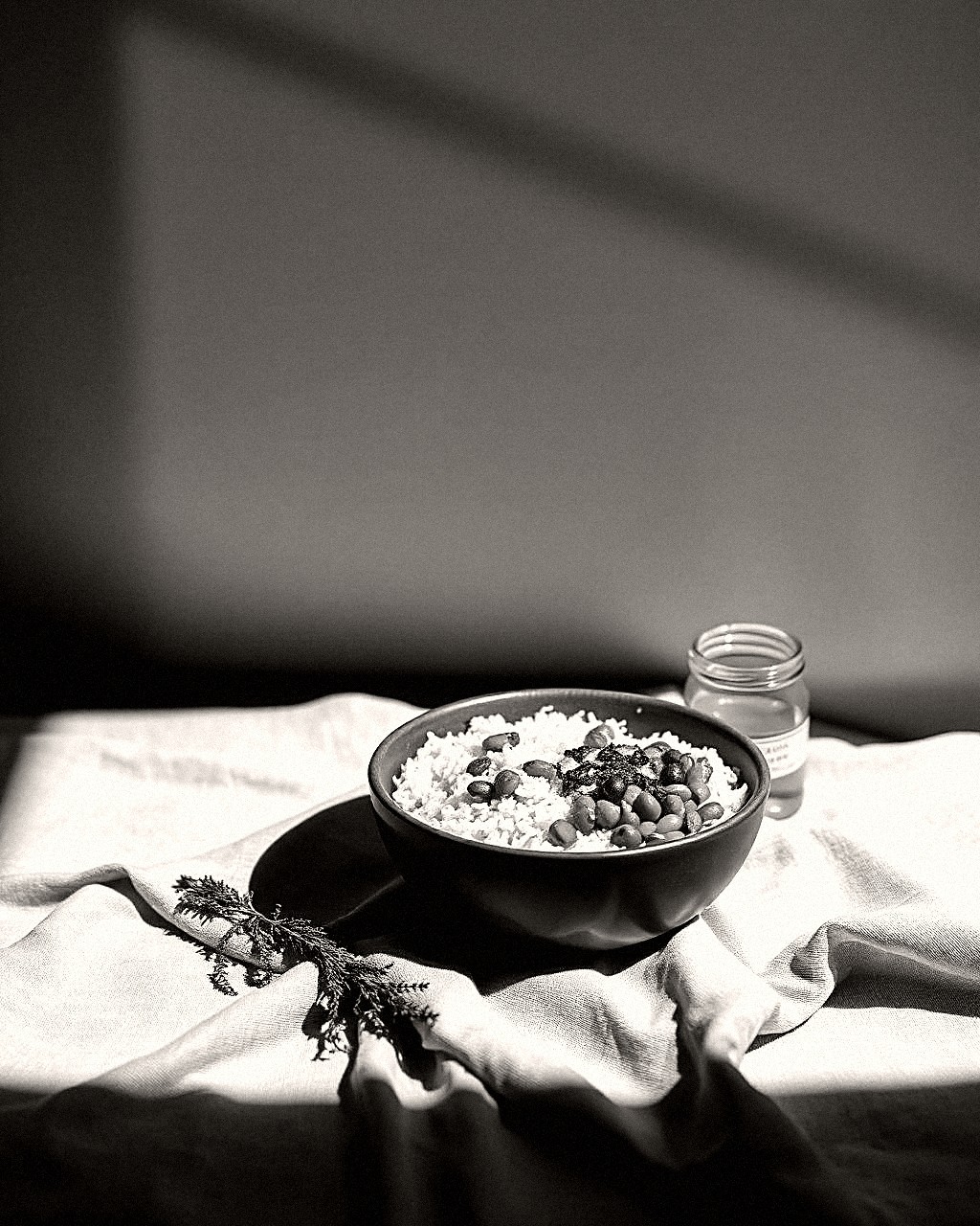 Black and white still life of a bowl of kitchari with a jar of ghee on linen