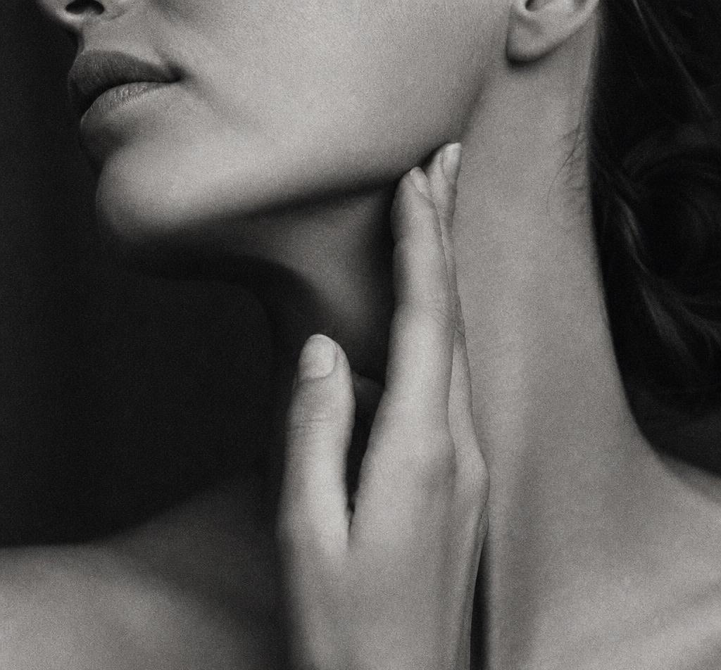 Black and white close-up of a woman's jawline and neck in a slow self-massage, overlaid with large art-deco type reading THE RITUAL OF TOUCH